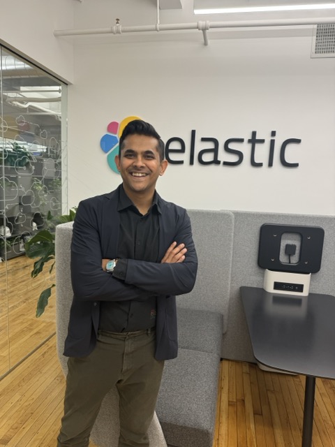 BK Bhate standing in front of an Elastic logo wall.