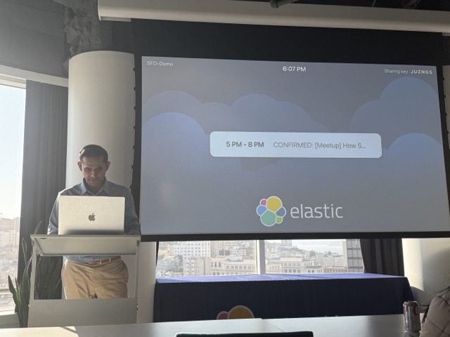 BK Bhate standing at a podium with an Elastic slide in the background.